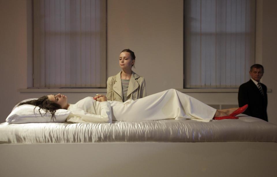 Visitors looks on a new art project called 'Sleeping Beauties' created by a Canadian-Ukrainian artist Taras Polataiko in The National Art Museum in Kiev, Ukraine, Friday, Sept. 7, 2012. Five young Ukrainian women, dressed in white wedding gowns, take turns sleeping on display in the museum for a couple of hours every day. Based on the fairytale 'Sleeping Beauty', the idea of the art-exhibition is for visitors to look at a sleeping girl, and, if they feel the urge, kiss her on the lips. If a sleeping beauty opens up her eyes she's obliged by a legal contract to marry. (AP Photo/Efrem Lukatsky)