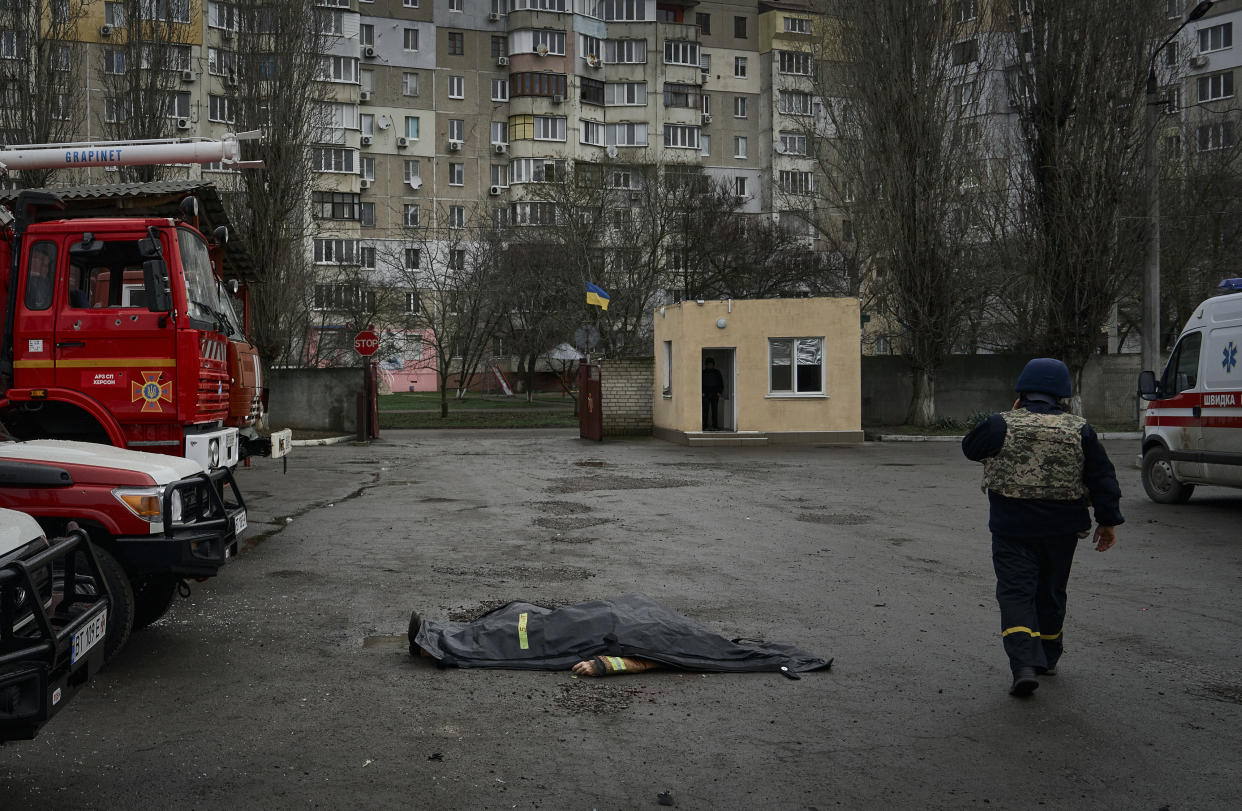 A firefighter passes by the dead body of a firefighter killed in the Russian shelling of the fire station in Kherson, Ukraine, on the Orthodox Christmas Eve Friday, Jan. 6, 2023. (AP Photo/LIBKOS)