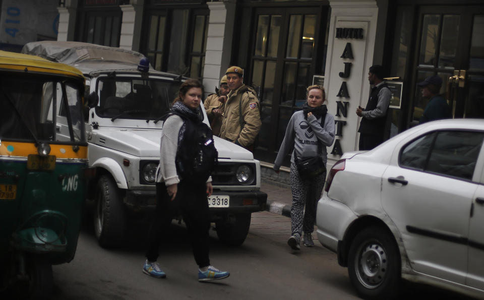 Foreign tourists walk past Delhi police officers in a neighborhood which houses hundreds of budget hotels in New Delhi, India, Wednesday, Jan. 15, 2014. A Danish tourist was gang-raped Tuesday evening near a popular central shopping area in the Indian capital after she lost her way and asked for directions back to her hotel, police said Wednesday. The attack is the latest case to focus international attention on the scourge of rape and violence against women in India. (AP Photo/Altaf Qadri)