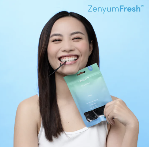 Young lady with the Zenyum Fresh Floss Picks in between her teeth and smiling.