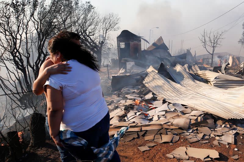 A woman and her son embrace next to the debris of their house as a fire continues in Valparaiso