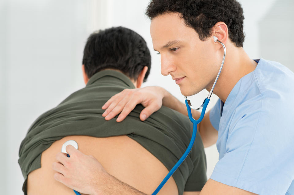 A male doctor listening to a man's heart with a stethoscope on his back