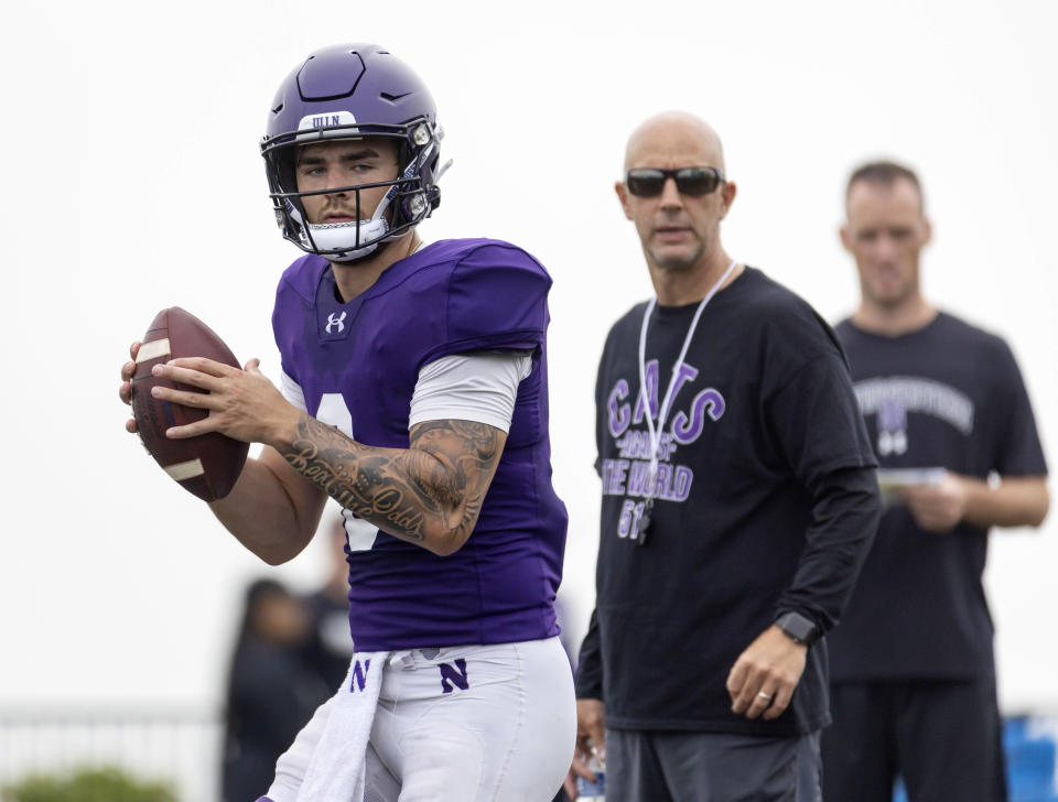 Northwestern quarterback Brendan Sullivan (6) throws in front of offensive coordinator Mike Bajakian during football practice Wednesday, Aug. 9, 2023, at Hutcheson Field in Evanston, Ill. Northwestern athletic director Derrick Gragg criticized assistant football coaches and staff members for wearing shirts supporting fired coach Pat Fitzgerald at practice Wednesday, calling them “inappropriate, offensive and tone deaf” given the hazing and abuse scandal engulfing the program and other teams.(Brian Cassella/Chicago Tribune via AP)