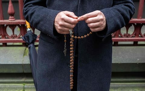 A supporter of Australian Cardinal George Pell prays while holding rosary beads outside the Supreme court of Victoria in Melbourne  - Credit: AFP