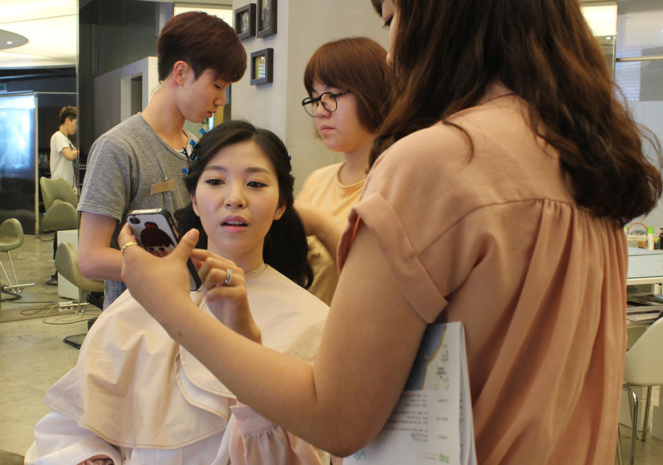 In this Tuesday, July 30, 2013 photo, Yang Candi of Beijing, China, points a photograph of a South Korean hairstyle on her smartphone at a hair salon in southern Seoul, South Korea, during a three-hour makeup session part of a South Korean wedding tourism package for Chinese couples. China is the source of one quarter of all tourists to South Korea, and a handful of companies in South Korea’s $15 billion wedding industry are wooing an image-conscious slice of the Chinese jet set happy to drop several thousand dollars on a wedding album with a South Korean touch. (AP Photo/Elizabeth Shim)