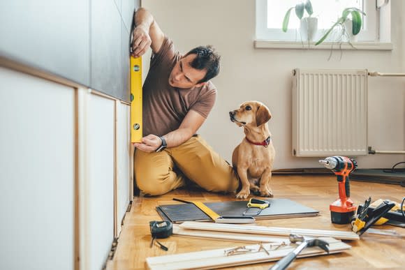 A man, next to his dog, working on a home improvement project.