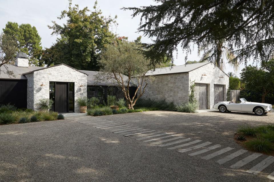 Inspired by a “funky barn in Sonoma,” designer Amber Lewis installed “old world meets modern” elements, like a corrugated metal roof in dark bronze paired with a Sherwin-Williams Tricorn Black front door, Shoppe Amber Interiors Darya Swan Neck wall lights in antique brass, stone siding, and a custom reclaimed wood garage door to welcome the vintage MG MKII car, a gift from Lewis’s late grandfather.
When you buy something through a retail link on Architectural Digest, we may earn an affiliate commission.