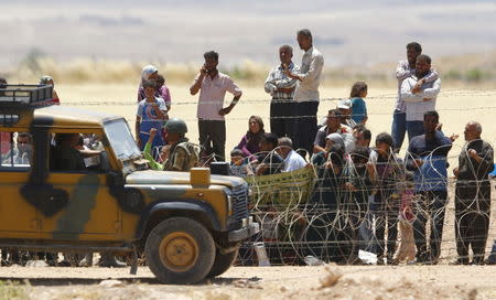 Syrian Kurds from Kobani wait behind the border fences to cross into Turkey as they are pictured from the Turkish border town of Suruc in Sanliurfa province, Turkey, June 26, 2015. REUTERS/Murad Sezer