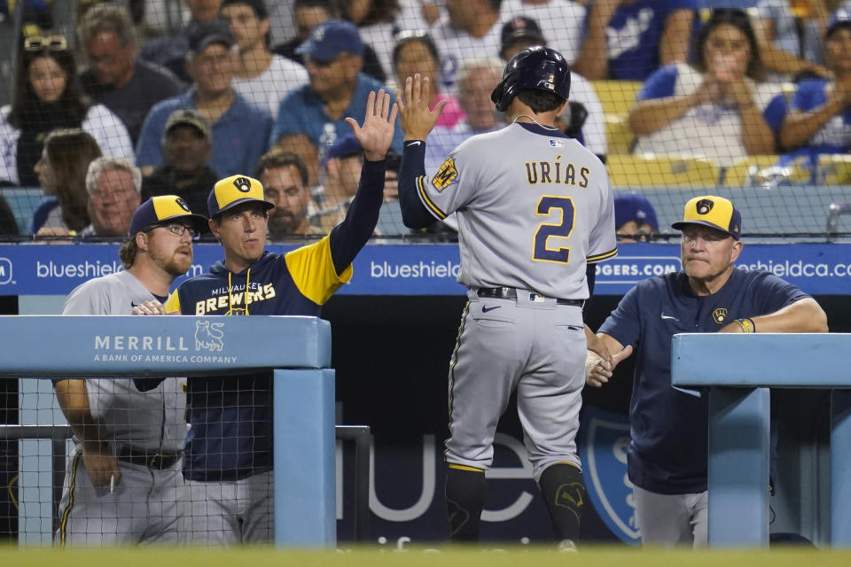 Milwaukee Brewers' Luis Urias (2) high-fives manager Craig Counsell, center left, after scoring off of a single hit by Jonathan Davis during the fifth inning of a baseball game against the Los Angeles Dodgers in Los Angeles, Tuesday, Aug. 23, 2022. (AP Photo/Ashley Landis)