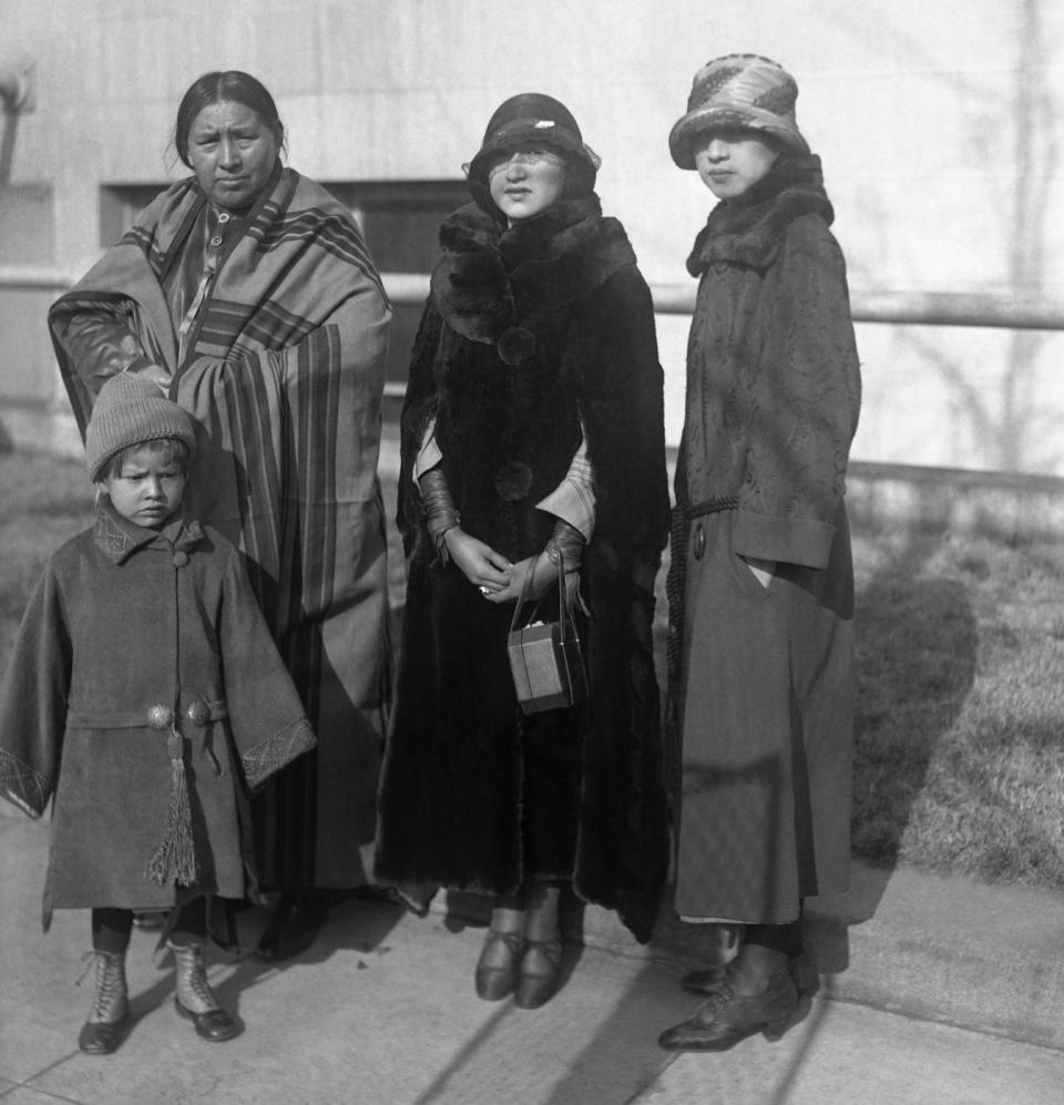 Two Indian flappers accompanied the group. Left to right in the group are Mrs. Red Eagle, Miss Rose Wagoshe, and Miss Mary Red Eagle. The child is little Miss Julia Red Eagle. The two young Indian girls, in their modern dress, present a striking comparison with the older Indian woman