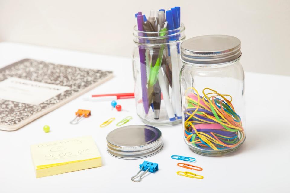 Clear Glass mason jars storing colorful office supplies on white desk