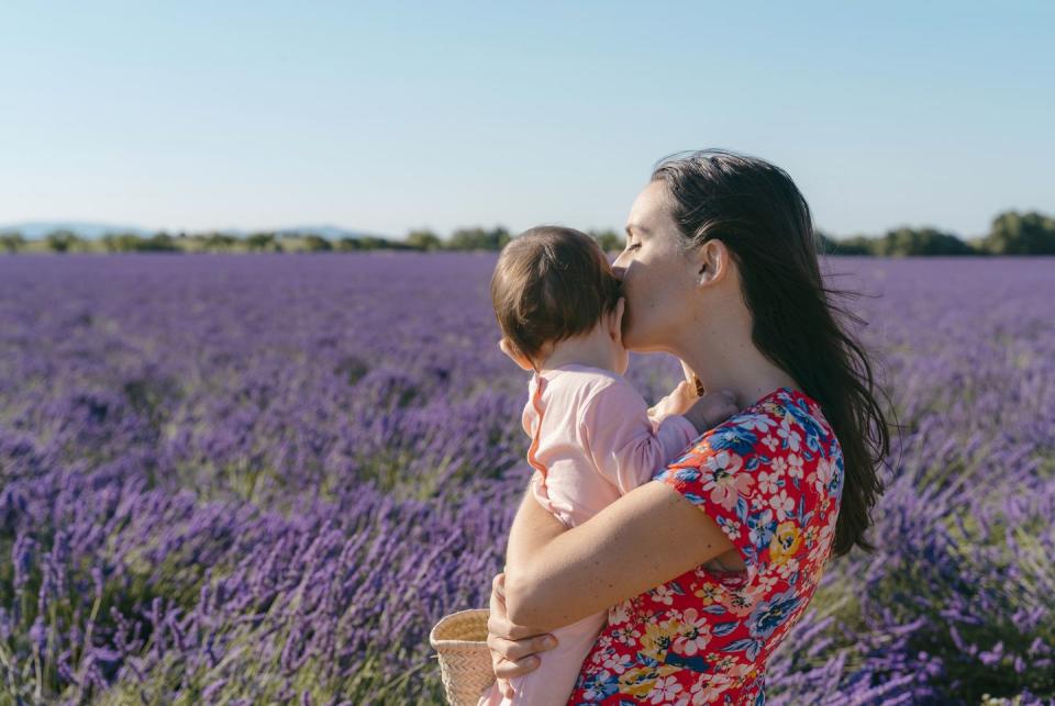 woman standing in vast lavender field with baby girl in hands
