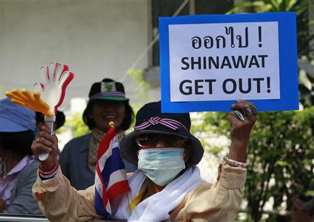 An anti-government protester uses a clapper while holding a placard during a rally on a main road leading towards the Government House in Bangkok December 9, 2013. REUTERS/Chaiwat Subprasom