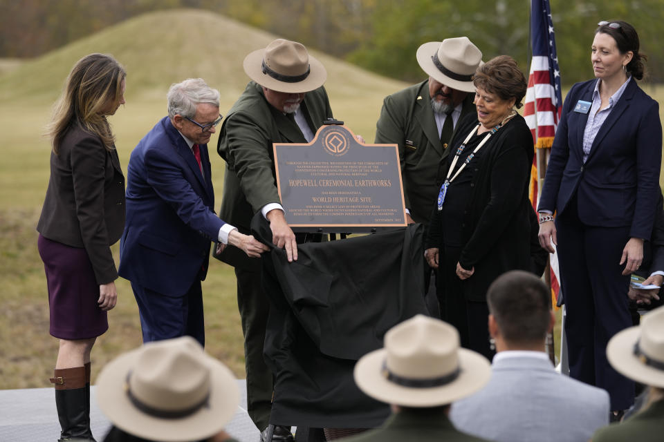 From left, Megan Wood, executive director of the Ohio History Connection; Ohio Gov. Mike DeWine; Chris Alford, superintendent of Hopewell Culture National Historical Park; National Park Service Director Chuck Sams; Chief Glenna Wallace, of the Eastern Shawnee Tribe of Oklahoma, and Jen Aultman of the Ohio History Connection, unveil a replica of a plaque during the Hopewell Ceremonial Earthworks UNESCO World Heritage Inscription Commemoration ceremony, at the Mound City Group at Hopewell Culture National Historical Park in Chillicothe, Ohio, Saturday, Oct. 14, 2023. A network of ancient American Indian ceremonial and burial mounds in Ohio noted for their good condition, distinct style and cultural significance, including Hopewell, was added to the list of UNESCO World Heritage sites. (AP Photo/Carolyn Kaster)