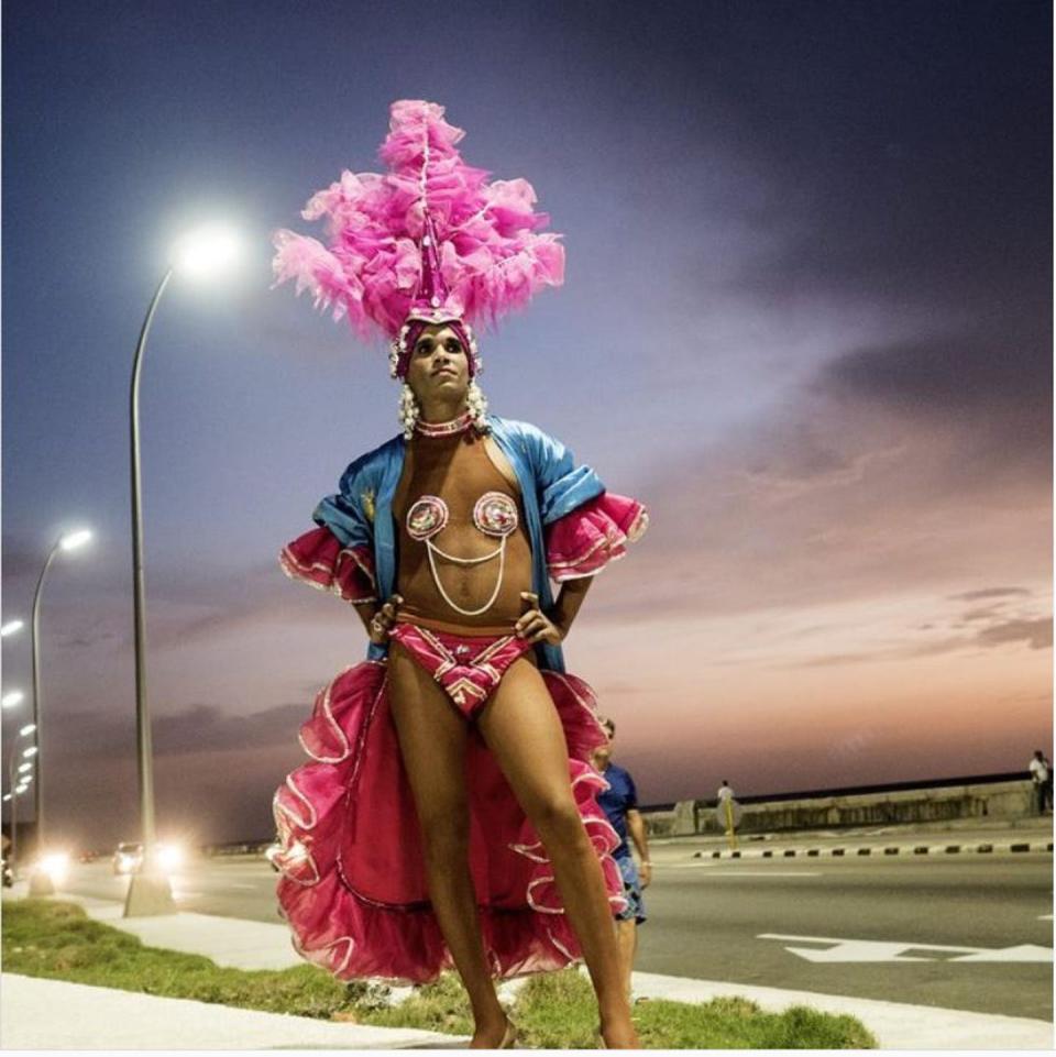 Man in a skimpy pink-feather outfit with a headress and cape