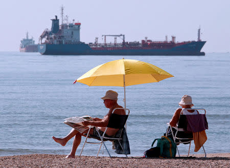 FILE PHOTO - People sunbathe as oil and gas tankers are anchored off the Fos-Lavera oil hub near Marseille, southeastern France, October 7, 2010. REUTERS/Jean-Paul Pelissier/File Photo