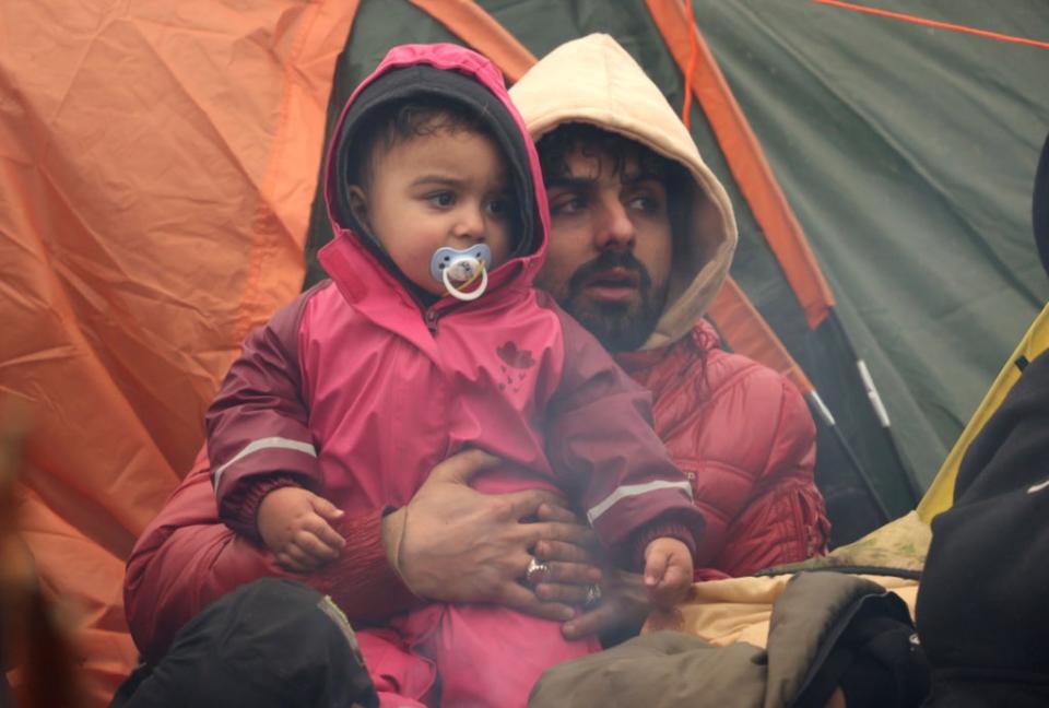 A man and his child try to stay warm inside a tent at the border near Grodno in Belarus (AP)