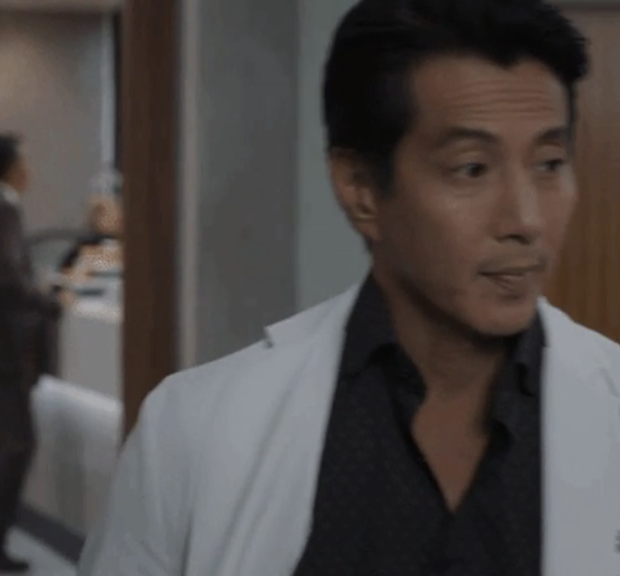 Man in a white blazer over a black shirt walking through an office setting
