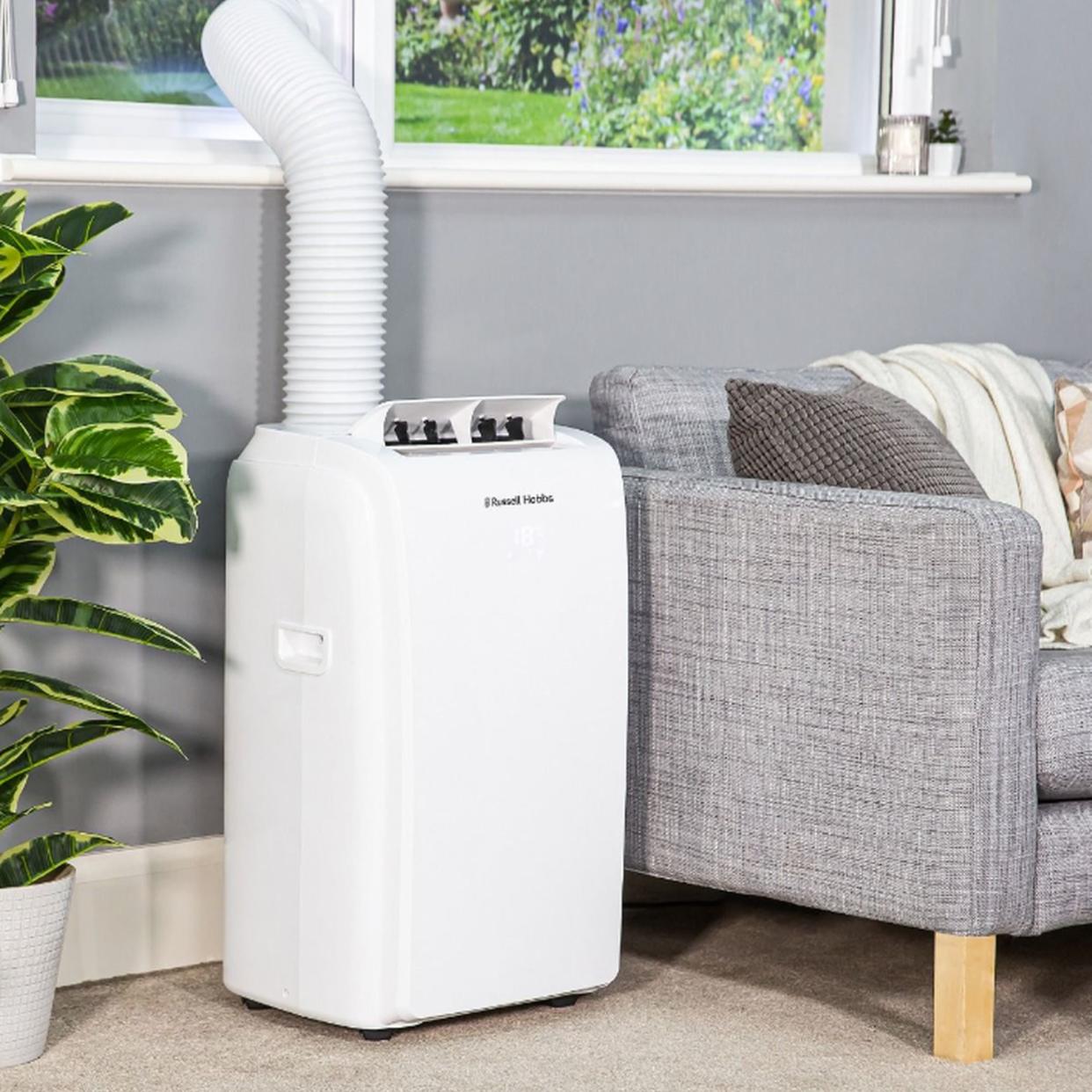  Russell Hobbs portable air conditioner next to grey couch. 