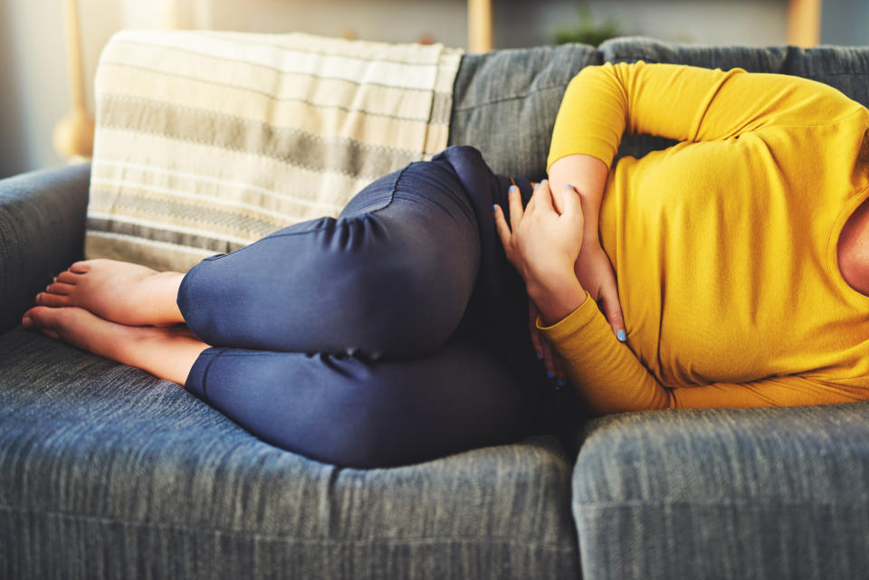 Cropped shot of a woman suffering from stomach cramps on the sofa at home