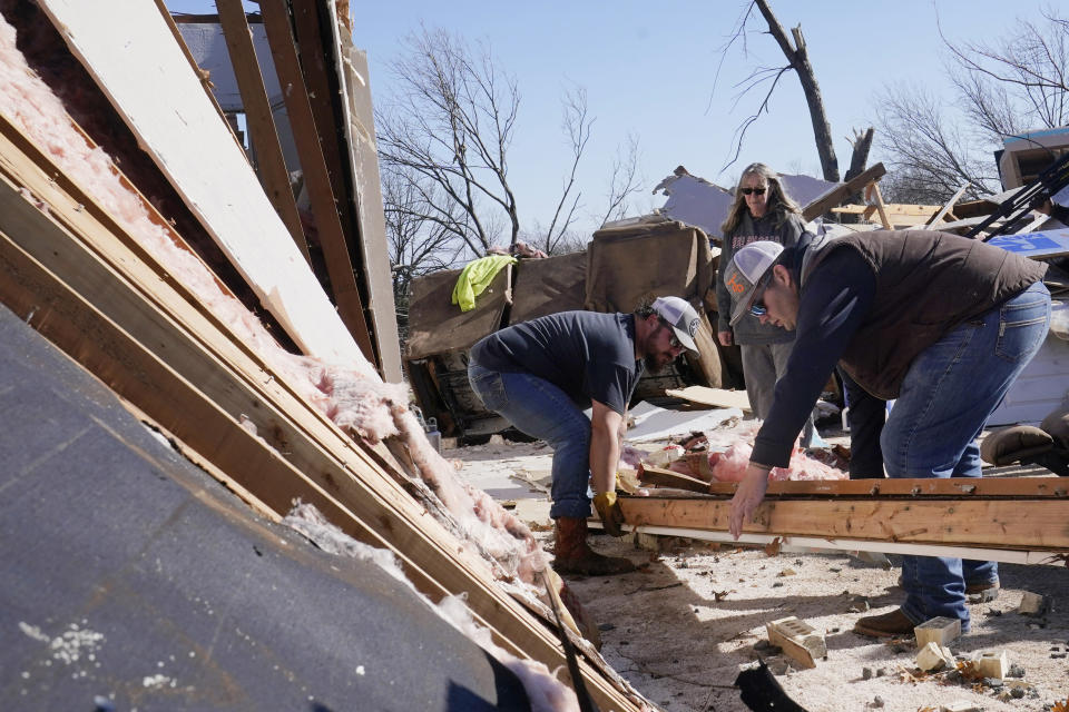 Belinda Penner, center, watches as Jr. Ibarra, left, and Jared Reaves, right, carry a beam from her cousin's tornado destroyed home, Tuesday, Dec. 13, 2022, in Wayne, Okla. (AP Photo/Sue Ogrocki)