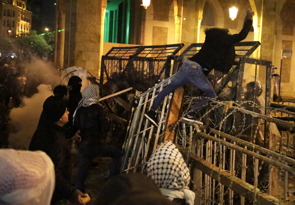 An anti-government protester stands on barriers defense as he throws stones against the riot police, during ongoing protests against the political elites who have ruled the country since decades, in Beirut, Lebanon, Sunday, Jan. 19, 2020. Lebanese security forces used tear gas, water cannons and rubber bullets in clashes with hundreds of anti-government protesters outside the country's Parliament on Sunday, as violence continued to escalate in a week of rioting in the capital. (AP Photo/Hassan Ammar)