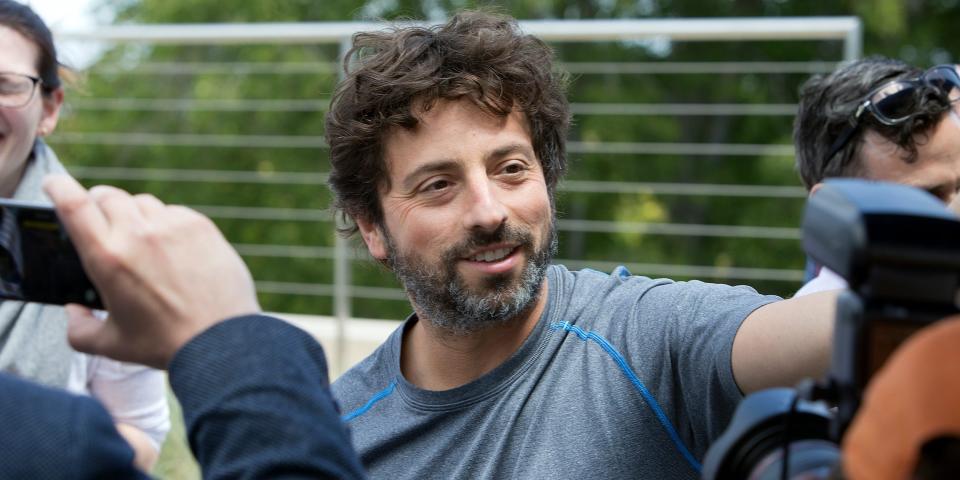 Sergey Brin looks off camera while surrounded by people taking photos of him