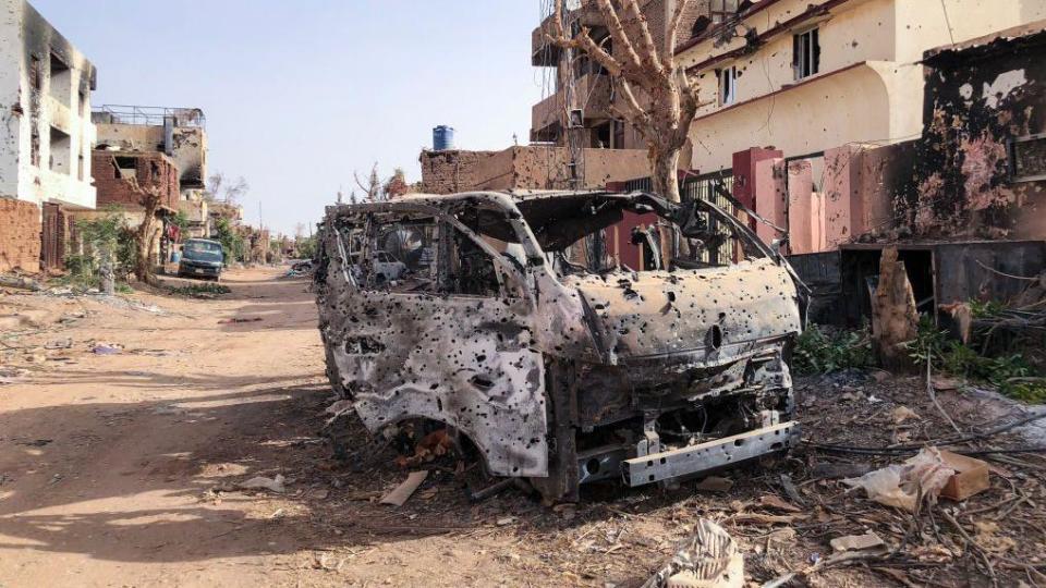 This photo taken on May 30, 2024 shows a burnt-out vehicle in front of a damaged shop in Omdurman