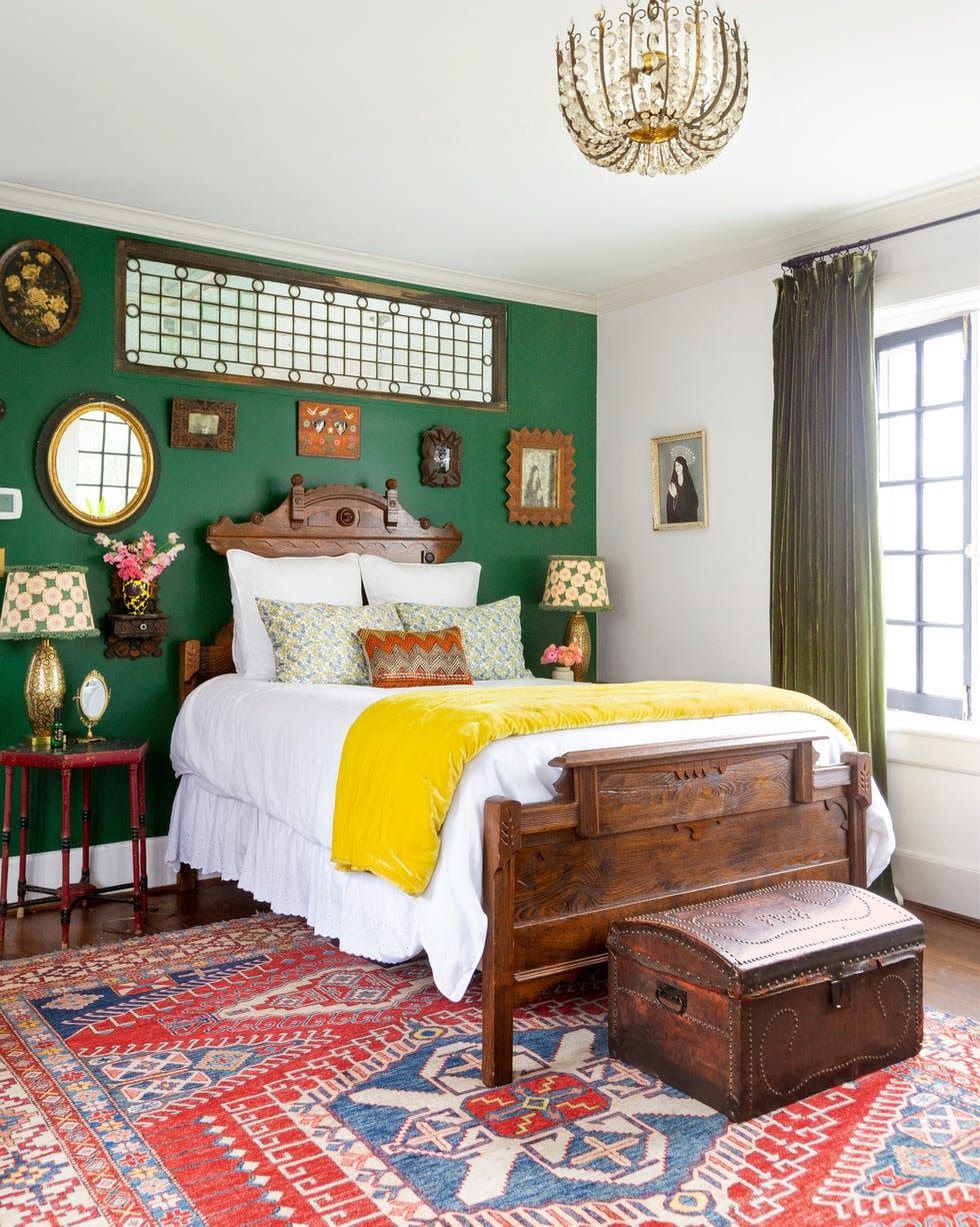 white bedroom with one clover green wall with wood bed and lots of art on wall