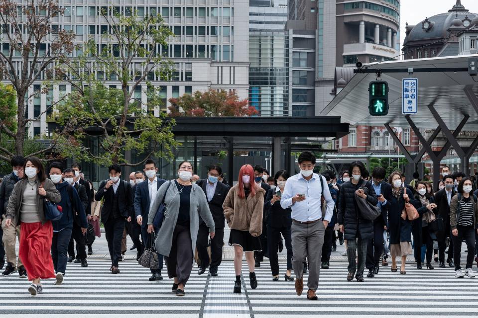 A large group of travellers and commuters crossing a road outside Tokyo station.