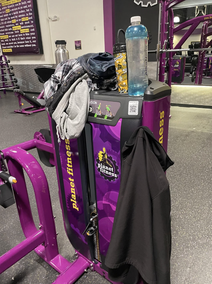 Various workout gear, including a water bottle, hoodie, and towel, placed on exercise equipment at Planet Fitness gym