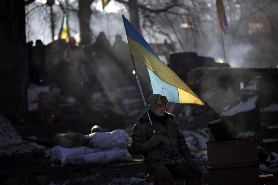 An opposition supporter holds an Ukrainian flag as he warms himself next to a fire in a barricade near Kiev's Independence Square, the epicenter of the country's current unrest, Ukraine, Friday, Jan. 31, 2014. Ukraine's embattled president Viktor Yanukovych is taking sick leave as the country's political crisis continues without signs of resolution. (AP Photo/Emilio Morenatti)