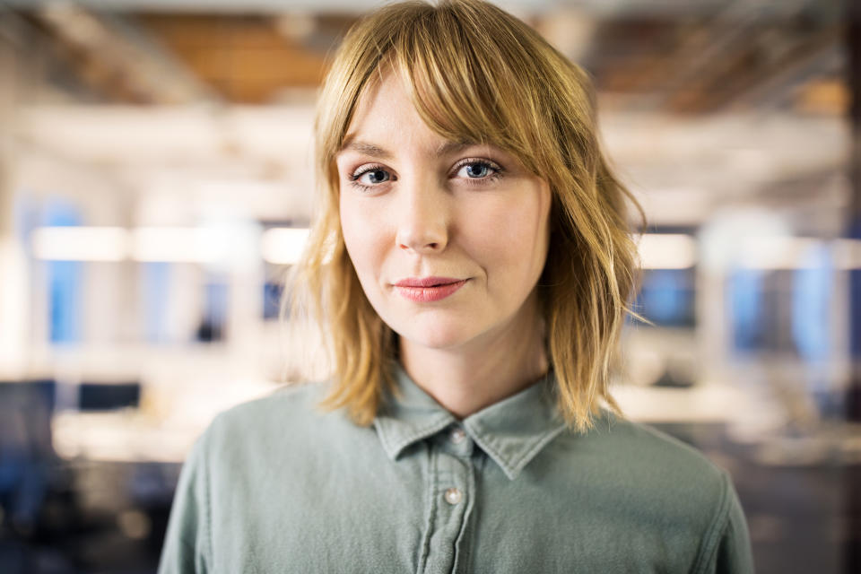 Close up portrait of young female businesswoman standing in modern office. 