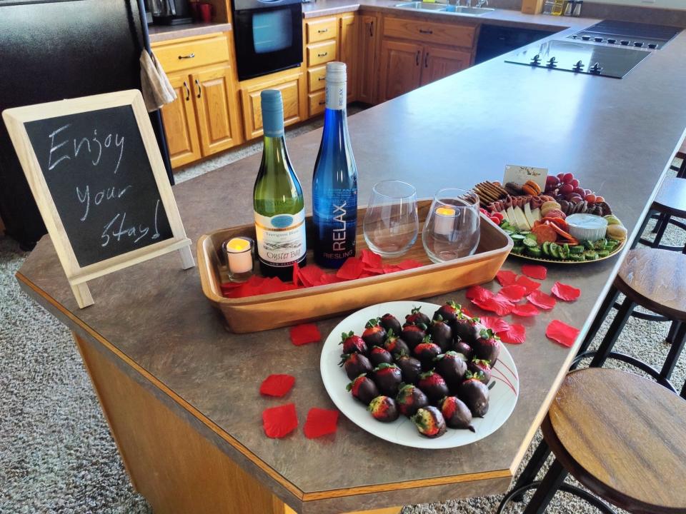 Bottles of wine, chocolate covered strawberries, and rose petals on a kitchen counter.