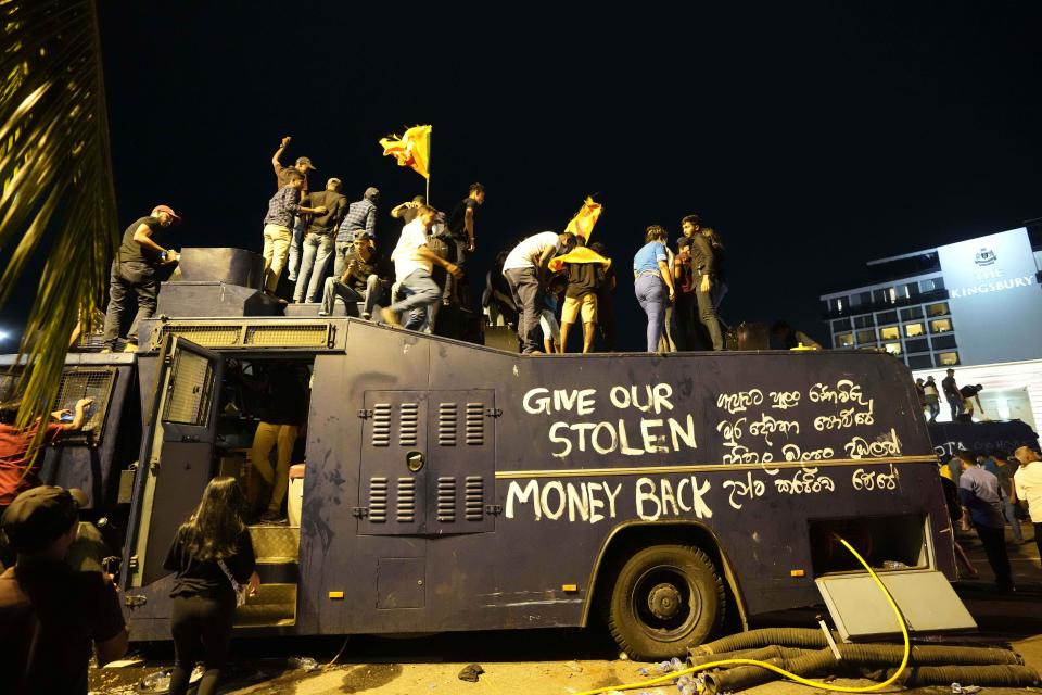 Protesters stand on a vandalised police water canon truck and shout slogans at the entrance to president's official residence in Colombo, Sri Lanka, Saturday, July 9, 2022. (AP Photo/Eranga Jayawardena)