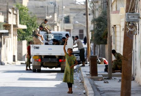 A girl carries water in a plastic can, with Turkish-backed Free Syrian Army (FSA) fighters in the background, in the border town of Jarablus, Syria. REUTERS/Umit Bektas