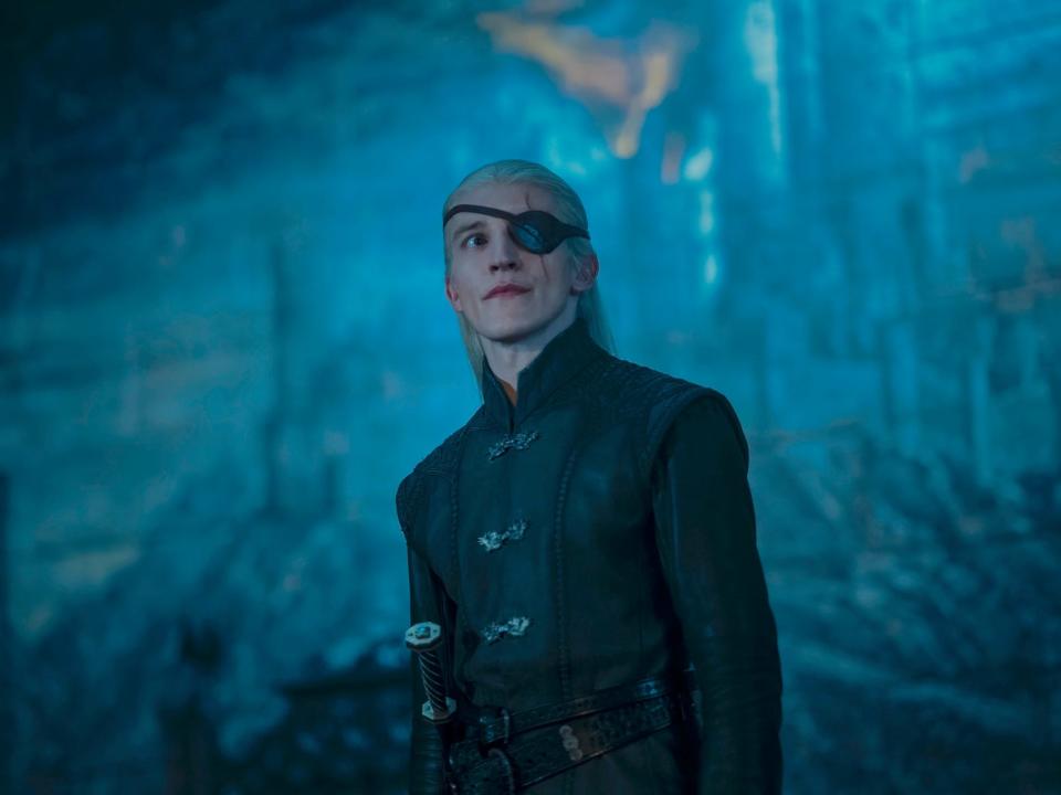 ewan mitchell as aemond targaryen in house of the dragon, wearing a black leather coat and with an eye patch strapped over his eye