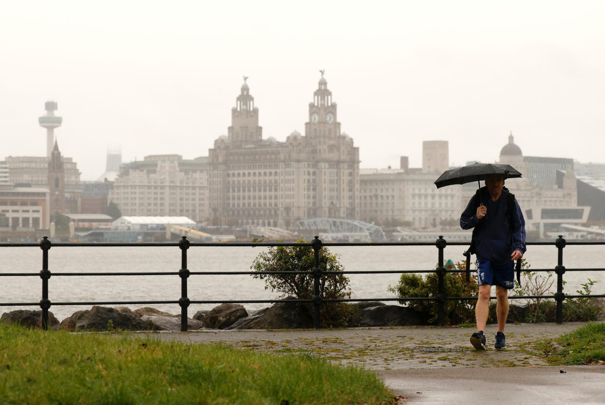 A man holds an umbrella as he walks along the River Mersey with the Liverpool skyline amid the outbreak of the coronavirus disease (COVID-19) in Seacombe, Britain, October 12, 2020. REUTERS/Phil Noble