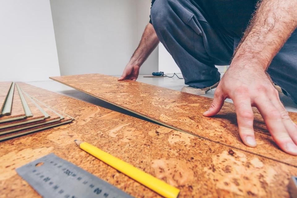 A close up of a man laying down cork flooring. 