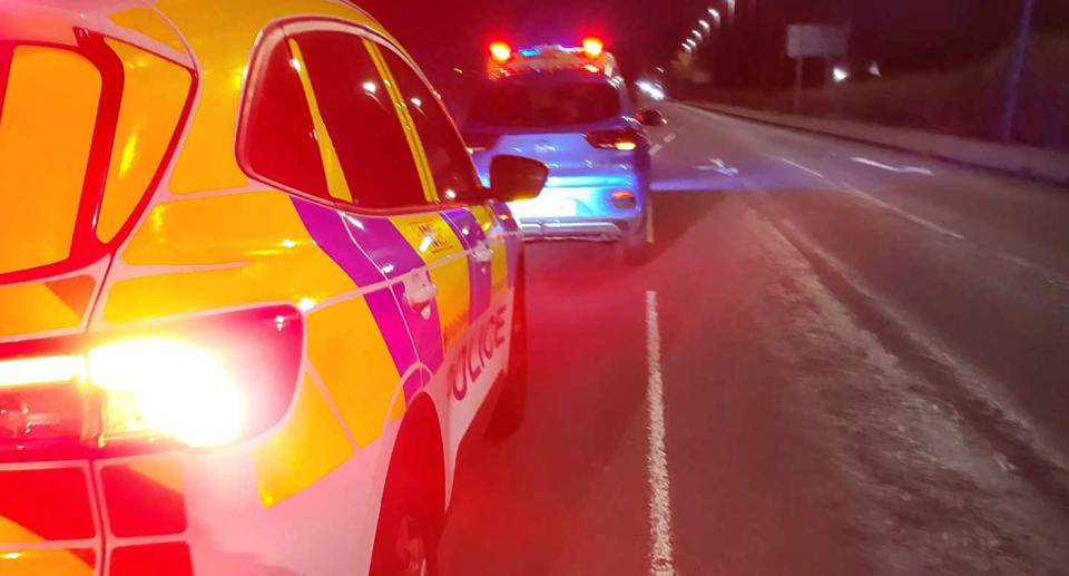 Police cars drive in front and behind the MG electric car in the dark.