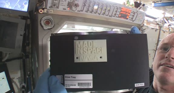 International Space Station commander Barry "Butch" Wilmore holds up the first 3D printed part made in space. The part, an extruder plate (a piece of the printer itself), was made on Nov. 24, 2014.