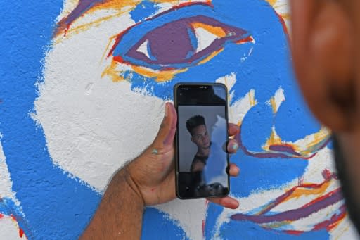 A friend of Cristian Charris looks at a photo on his cell phone as he paints a mural of his dead friend at a basketball court where a tournament was played in his honor