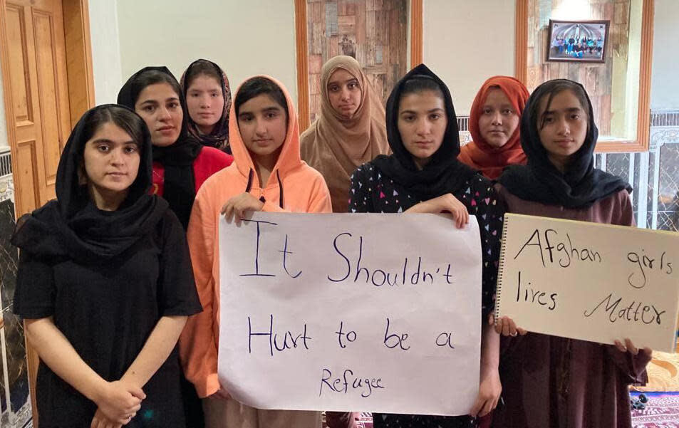 A group of Afghan girls who perform as musicians in Pakistan, known as the Miraculous Love Kids, hold signs saying 