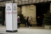 A woman wearing a face mask walks past Christmas trees and a social distancing sign outside the Selfridges department store on Oxford Street, which is temporarily closed for in-store browsing with online collection possible from a collection point, during England's second coronavirus lockdown, in London, Monday, Nov. 23, 2020. British Prime Minister Boris Johnson has announced plans for strict regional measures to combat COVID-19 after England's second lockdown ends Dec. 2, sparking a rebellion by members of his own party who say the move may do more harm than good. (AP Photo/Matt Dunham)