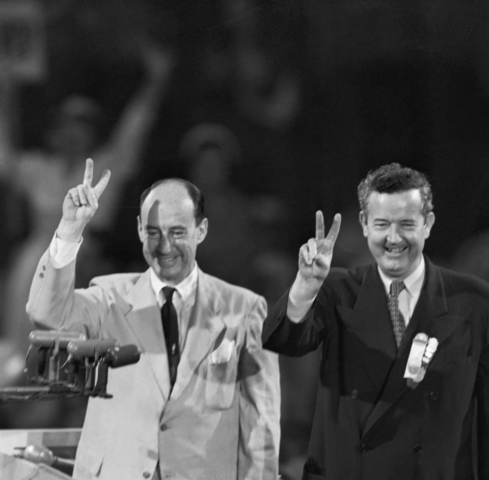 Two men in suits and ties making V signs to a crowd.