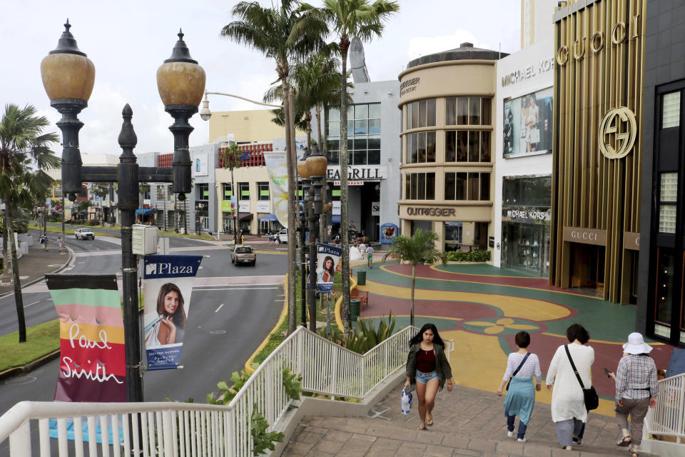 FILE - Tourists walk through a shopping district in Tamuning, Guam on May 15, 2017. The powerful Pacific typhoon Mawar that lashed of Guam on Thursday, May 25, 2023, with damaging high winds, heavy rains and a dangerous storm surge arrived as the worst storm in decades, interrupting life for residents and the U.S. military on a tropical island that is the easternmost of the nation's territories. (AP Photo/Haven Daley, File)