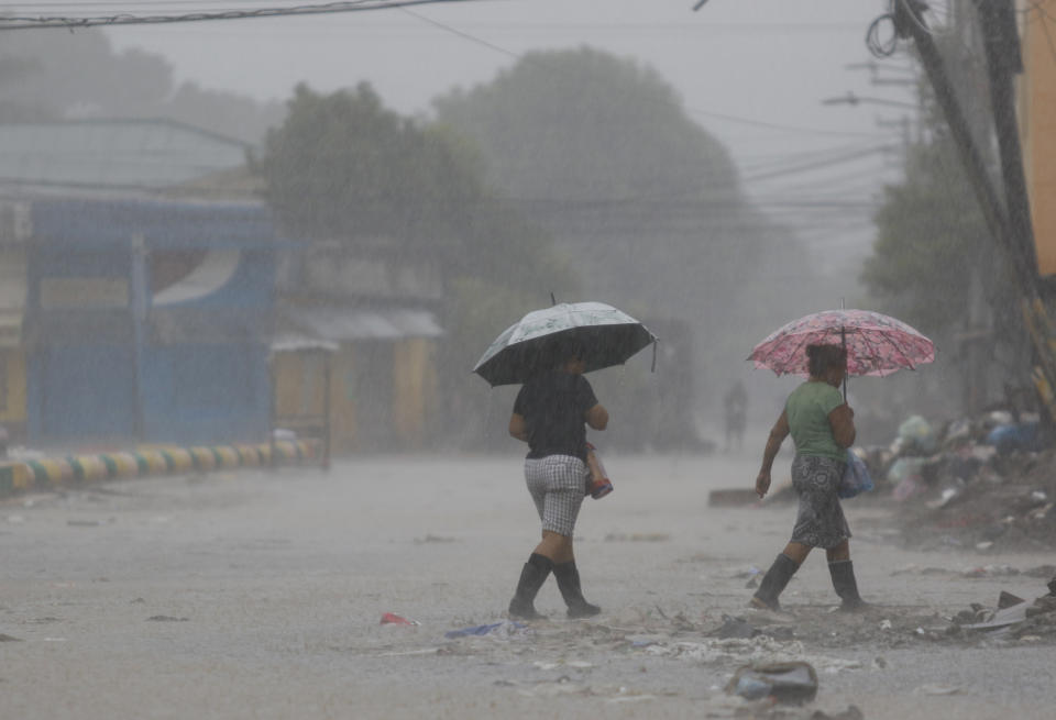 Women walk under in the rain brought by Hurricane Iota, in La Lima, Honduras, Tuesday, Nov. 17, 2020. Hurricane Iota tore across Nicaragua on Tuesday, hours after roaring ashore as a Category 4 storm along almost exactly the same stretch of the Caribbean coast that was recently devastated by an equally powerful hurricane. (AP Photo/Delmer Martinez)