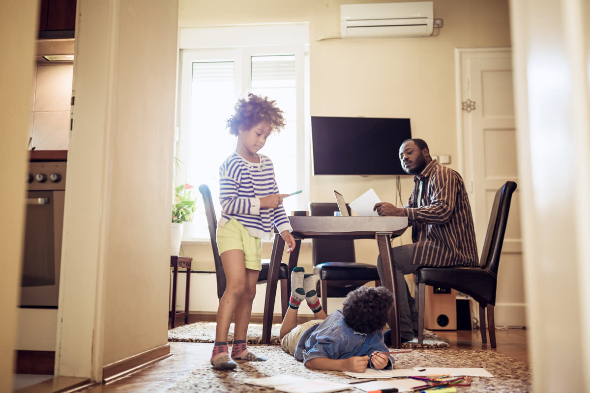 This photo shows a father working from home with his children coloring. 