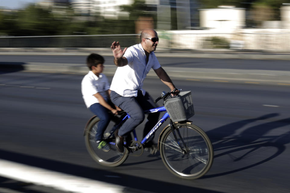 In this Wednesday, July 24, 2019 photo, a Syrian man rides a bike with his son on a bridge in the Syrian capital, Damascus. Syrians say it’s even harder now to make ends meet than it was during the height of their country’s civil war because of intensified U.S and European sanctions. Prices have leaped because of restrictions on oil imports, the value of the currency has plunged in recent months. Most of the country is now below the poverty line, earning less than $100 a month. (AP Photo/Hassan Ammar)