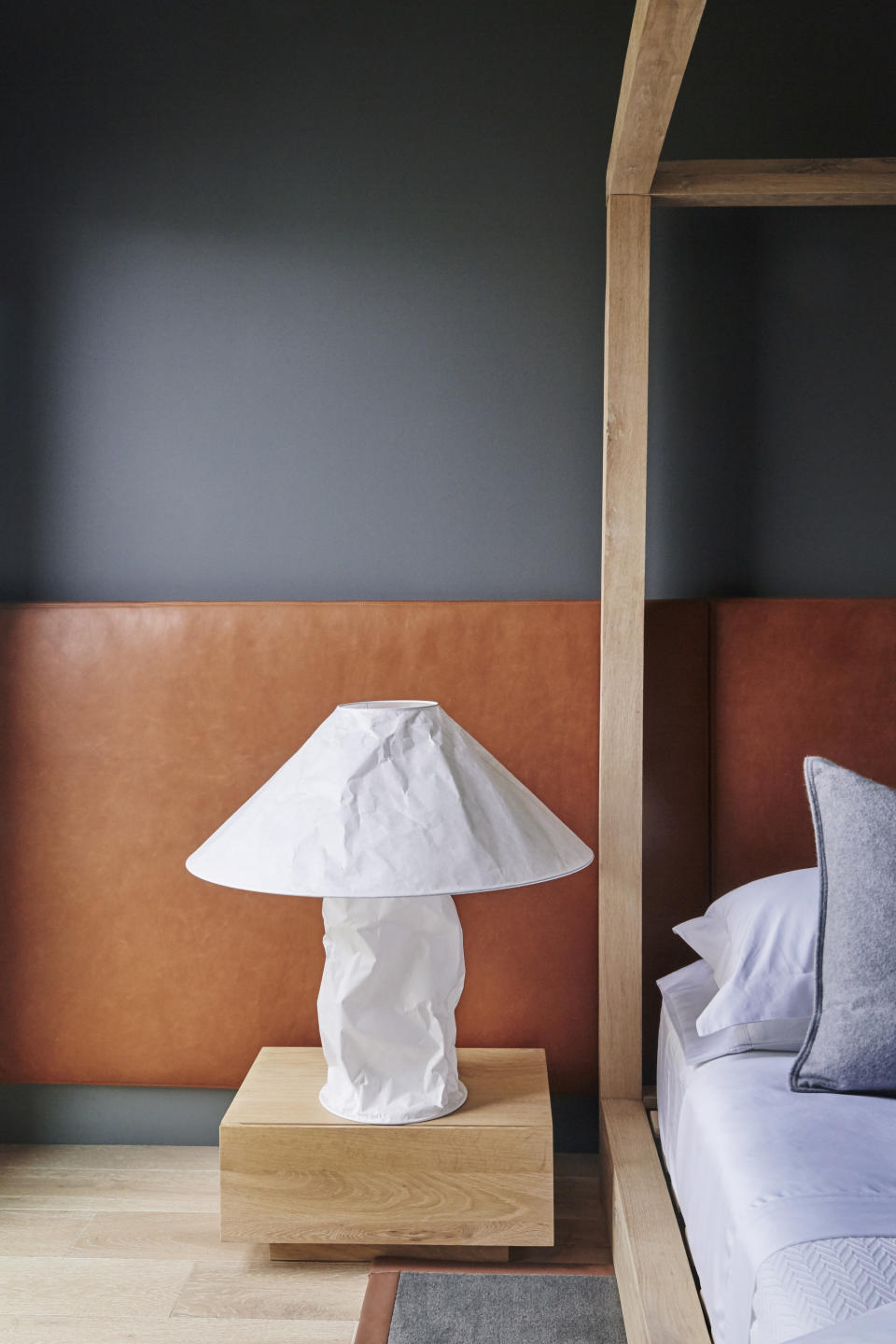 A bedroom with dark grey walls and tan headboard